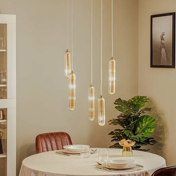 Lucande Pendelleuchte Freylin - L x B x H: 48 x 48 x 170 cm, creme / amber, amber, messing, G9 - Fünf zylindrische Pendelleuchten aus bernsteinfarbenem Glas hängen über einem gedeckten Esstisch. Sie spenden warmes, dekoratives Licht.