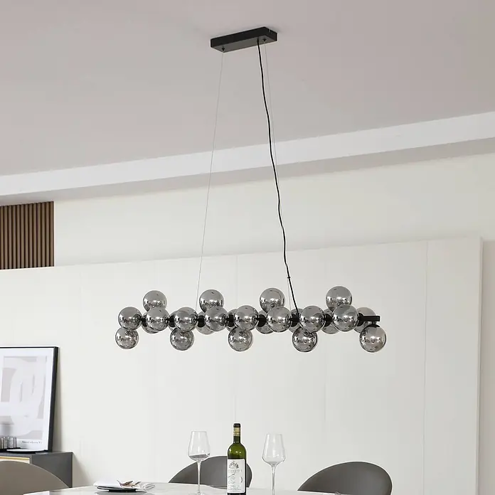 Lucande Pendelleuchte Naelen - alu / grau / zink, Schwarz, rauchgrau, G9 - Ein moderner Kronleuchter mit zahlreichen reflektierenden Kugel-Leuchten, aufgehängt über einem Esstisch.