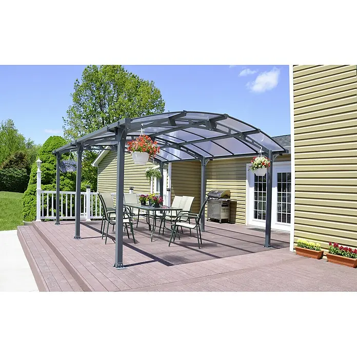 Palram – Canopia Carport Arcadia 5000 - Außenmaß inkl. Dachüberstand (B x T): 3,59 x 3,59 m, Doppelcarport, Grau - Hier ist eine graue Terrassenüberdachung mit Tisch und Stühlen im Freien, umgeben von Grün und einem beigen Haus.