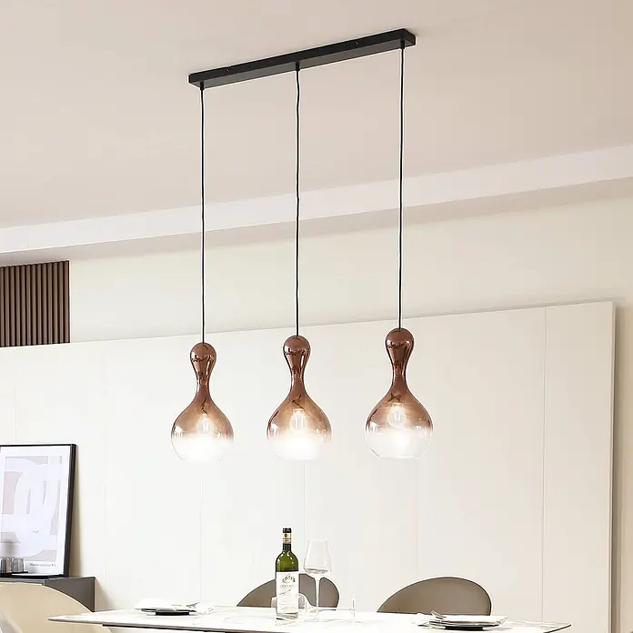 Lucande Pendelleuchte Lyrisa - kupfer, Kupfer, Schwarz, E27 - Drei Pendelleuchten mit kupferfarbenen Oberteilen und klaren Glasböden, die von einer schwarzen Stange hängen und warmes Licht über einem Esstisch abgeben.