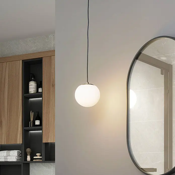 Lucande Pendelleuchte Bidolo - L x B x H: 15 x 15 x 13,5 cm, messingfarben, E14 - Weiße Glaskugel-Pendelleuchte mit goldener Fassung, an schwarzem Kabel hängend, beleuchtet ein modernes Badezimmer.