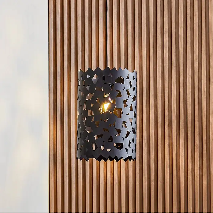 Lucande Pendelleuchte Aeloria - L x B x H: 25 x 25 x 37,5 cm, schwarz, Schwarz, E27 - Schwarze Metall-Hängeleuchte mit geometrischem Ausschnittmuster, beleuchtet, vor einer Holzlamellenwand.