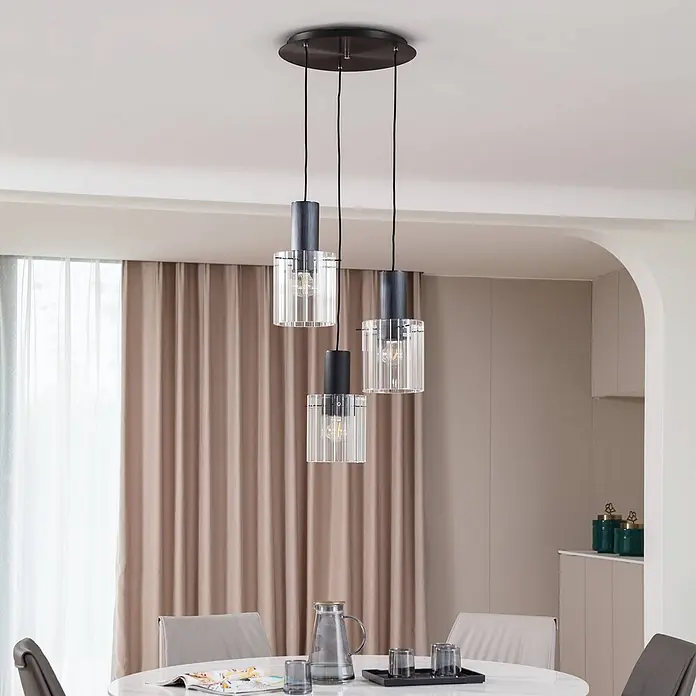 Lucande Pendelleuchte in transparent, schwarz, Hängelampe -  - Drei schwarze Pendelleuchten aus Metall und gerilltem Klarglas über einem Esstisch.