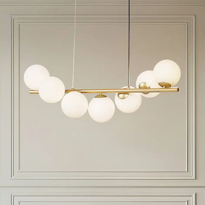 Lucande Pendelleuchte Isandro - L x B x H: 95 x 33 x 33 cm, gold matt, opal, G9 - Goldfarbener Kronleuchter mit mehreren weißen kugelförmigen Glasschirmen, an der Decke hängend.