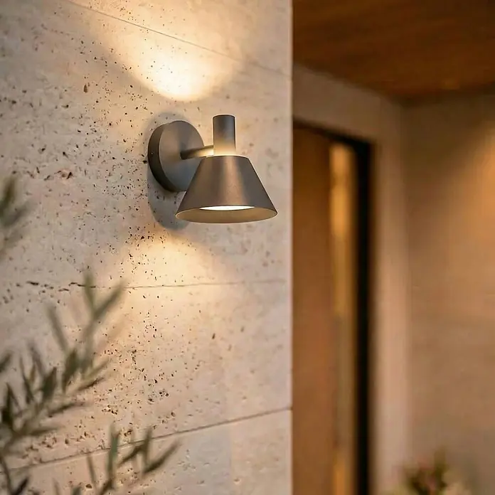 Lucande Außenwandleuchte Tabena - schwarz, schwarz, IP54 - Dunkelgraue Metall-Wandleuchte mit konischem Schirm beleuchtet eine strukturierte Steinwand.