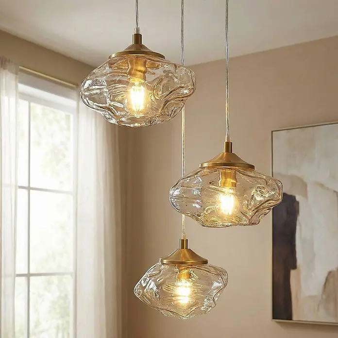 Lindby Pendelleuchte Piatra - L x B x H: 25 x 25 x 150 cm, creme / amber, amber, messing, G9 - Drei Hängeleuchten mit strukturierten Klarglasschirmen und Messingakzenten hängen beleuchtet von der Decke.