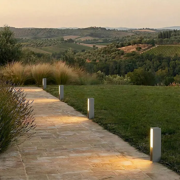 Lucande Außensockelleuchte Teerk -  - Graue, rechteckige Wegeleuchten beleuchten einen Ziegelweg in einer malerischen Gartenlandschaft.