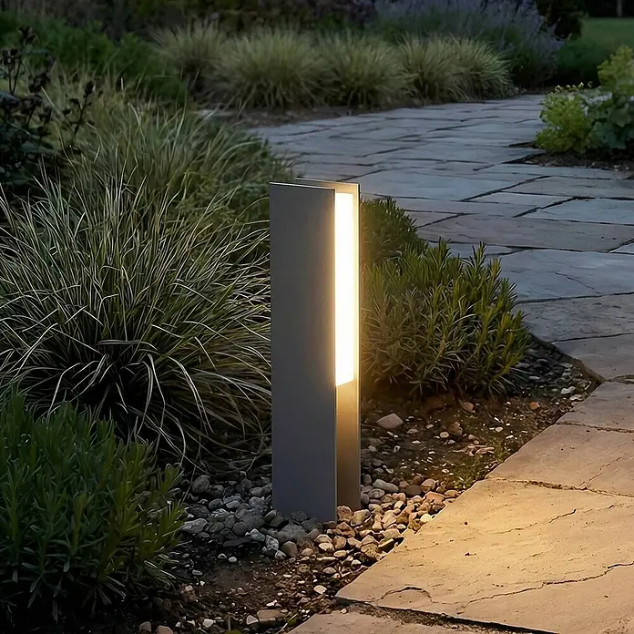 Lucande Außensockelleuchte Teerk -  - Moderne dunkelgraue Wegeleuchte beleuchtet einen Gartenweg mit Pflanzen.