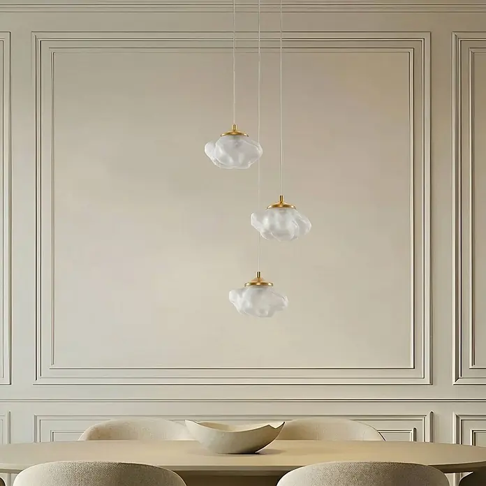 Lindby Pendelleuchte Piatra - weiß / opal, weiß, messing, G9 - Drei wolkenförmige Pendelleuchten mit mattem Glasschirm und Goldakzenten hängen über einem Esstisch.