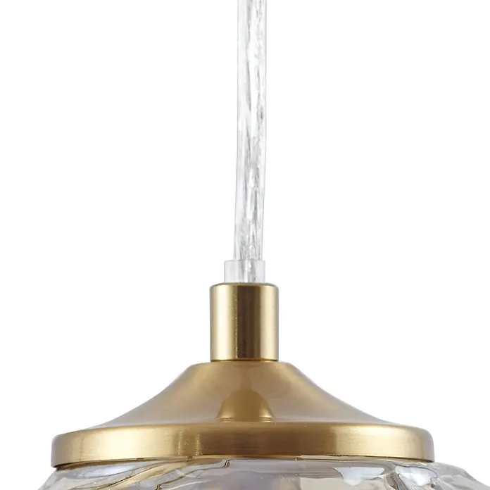 Lindby Pendelleuchte Piatra - L x B x H: 15,5 x 15,5 x 8,5 cm, creme / amber, amber, messing, G9 - Nahaufnahme einer Pendelleuchte mit transparentem Kabel und gebürstetem Goldmetallgehäuse, verbunden mit einem klaren, strukturierten Glasschirm.