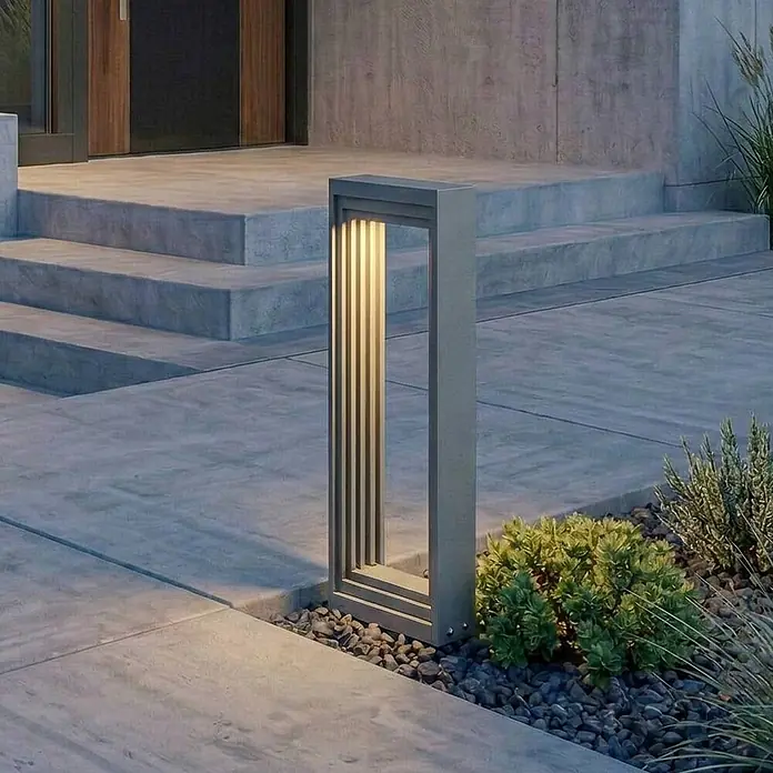 Lucande Außensockelleuchte Ashkan -  - Moderne graue Metall-Pollerleuchte beleuchtet Betonweg neben Stufen und Grün.