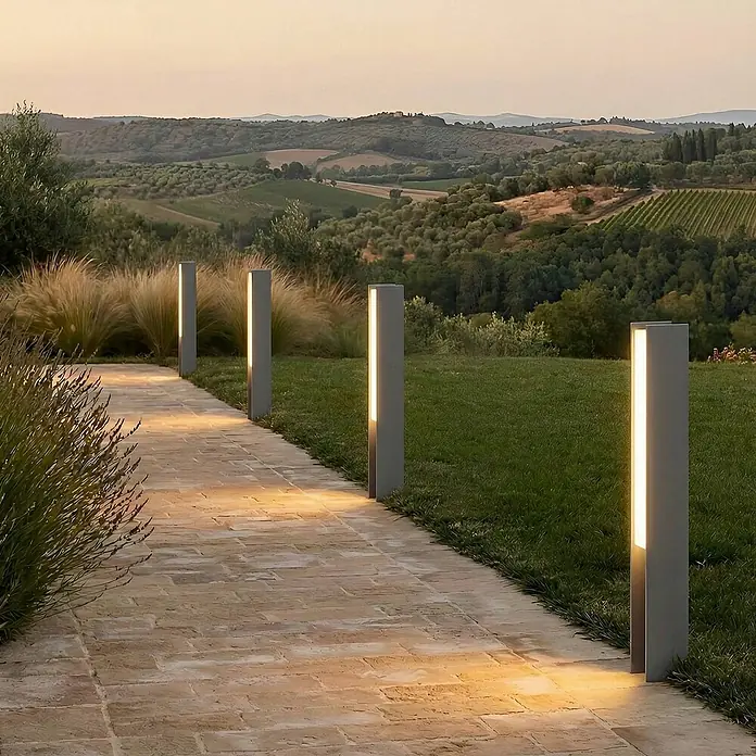 Lucande LED Sockelleuchte in schwarz, Wegeleuchten außen -  - Graue, rechteckige Pollerleuchten beleuchten einen gepflasterten Gartenweg in einer hügeligen Landschaft bei Dämmerung.