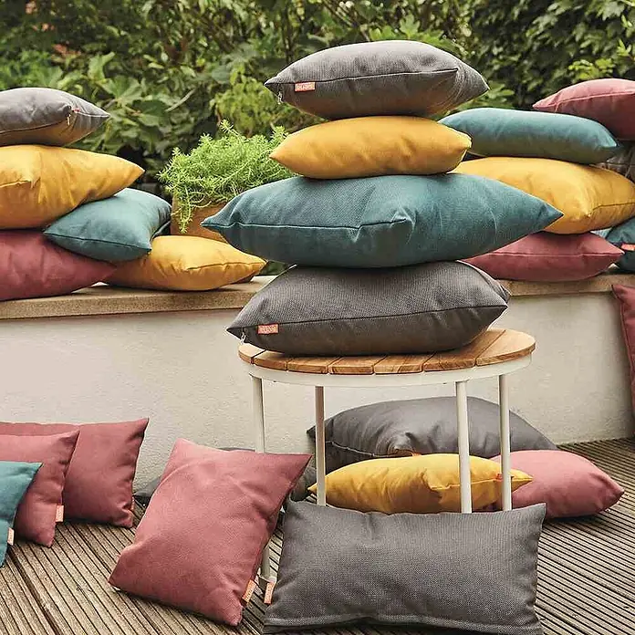 Siena Garden Kissen PRIME - 45 x 45 cm, Petrol, Quadratisch - Mehrere strapazierfähige Outdoor-Kissen in Dunkelgrau, Senfgelb, Petrol und Altrosa, auf einer Terrasse arrangiert.