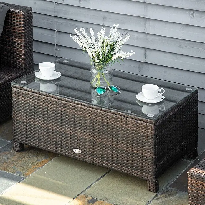 Outsunny Garten-Loungetisch - Metall, PE-Rattan, gehärtetes Glas, Braun, L x B x H: 85 x 50 x 39 cm - Brauner Rattan-Couchtisch mit Glasplatte, dekoriert mit Blumen und Tassen auf einer Terrasse.