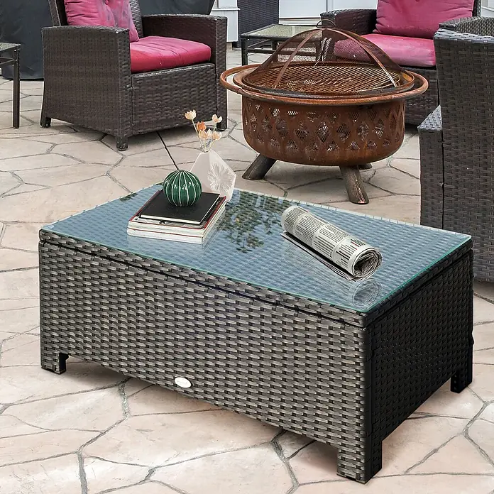 Outsunny Garten-Loungetisch im Rattan-Design - Metall, PE-Rattan, gehärtetes Glas, Schwarz, L x B x H: 85 x 50 x 39 cm - Rechteckiger Terrassen-Couchtisch mit dunkelgrauem Rattan-Geflecht und Glasplatte auf einer Steinterrasse.