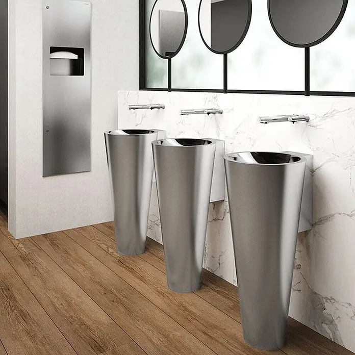 Delabie Waschbecken Delabie - Hahnloch: Ohne, Ohne Überlauf, Edelstahl - Drei elegante Waschtischsäulen aus gebürstetem Metall mit Wandarmaturen in einer modernen öffentlichen Toilette.