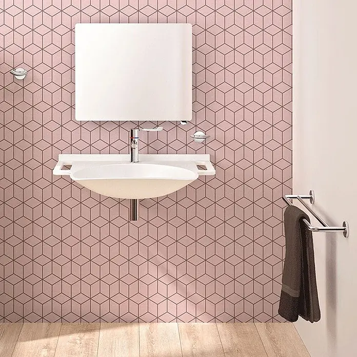 Delabie Waschbecken Delabie - Mit Überlauf, Weiß - Modernes weißes Badezimmerwaschbecken mit Chromarmatur und Spiegel an einer rosa geometrischen Wand. Ein Handtuch hängt an einem Halter.
