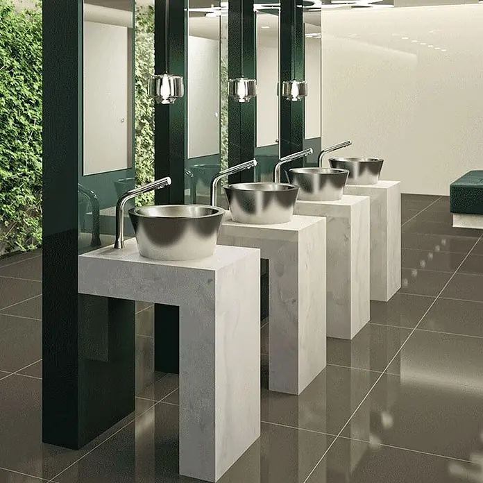 Delabie Spültischarmatur Delabie - Chrom - Vier moderne Waschtische mit Edelstahlbecken und eleganten Armaturen auf minimalistischen weißen Sockeln in einer modernen öffentlichen Toilette.
