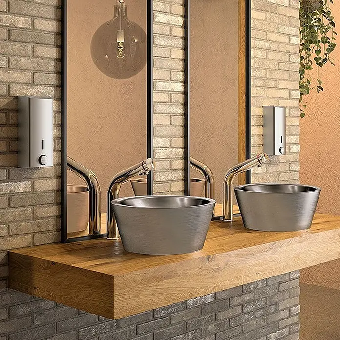 Delabie Waschbecken Delabie - Chrom - Zwei Waschbecken aus gebürstetem Metall mit Goldarmaturen auf einer Holzplatte im modernen Bad.