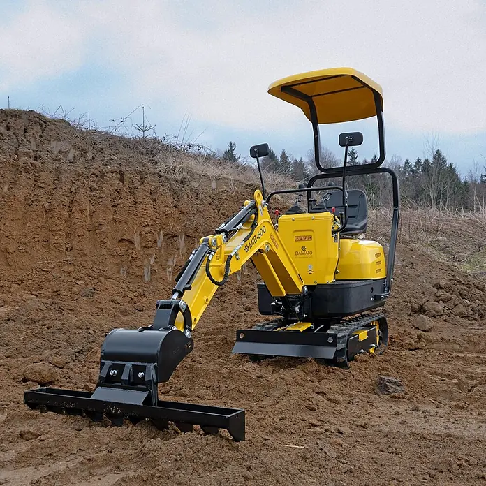 Bamato Minibagger MIB-600 - 6.300 W, Benzin, Auslegerschwenkbereich: 70 ° - Gelber und schwarzer Minibagger mit Rechenaufsatz auf einer Erdaushubstelle.