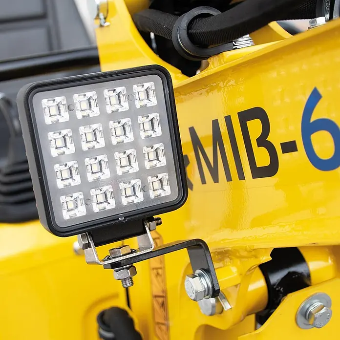 Bamato Minibagger MIB-600 - 6.300 W, Benzin, Auslegerschwenkbereich: 70 ° - Quadratische schwarze LED-Arbeitsleuchte mit 16 LEDs, montiert mit einer Metallhalterung an einer gelben Baumaschine.