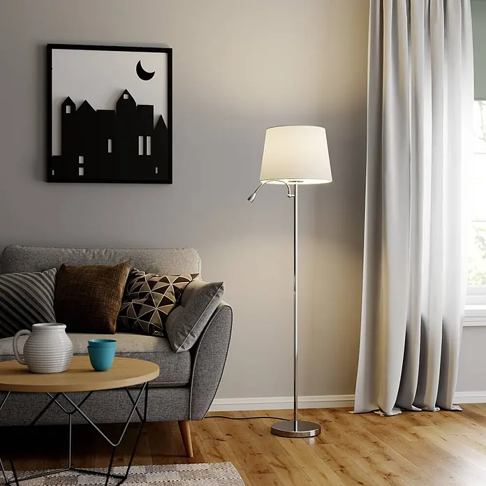 Lindby Stehleuchte Benjiro - chrom / silber, weiß / opal, E27 - Eine moderne Stehlampe aus Chrom mit weißem Schirm und verstellbarer Leselampe beleuchtet ein gemütliches Wohnzimmer neben einem grauen Sofa.