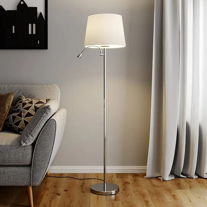 Lindby Stehleuchte Benjiro - chrom / silber, weiß / opal, E27 - Stehleuchte aus Chrom mit weißem Stoffschirm und verstellbarer Leselampe, neben einem Sofa platziert.