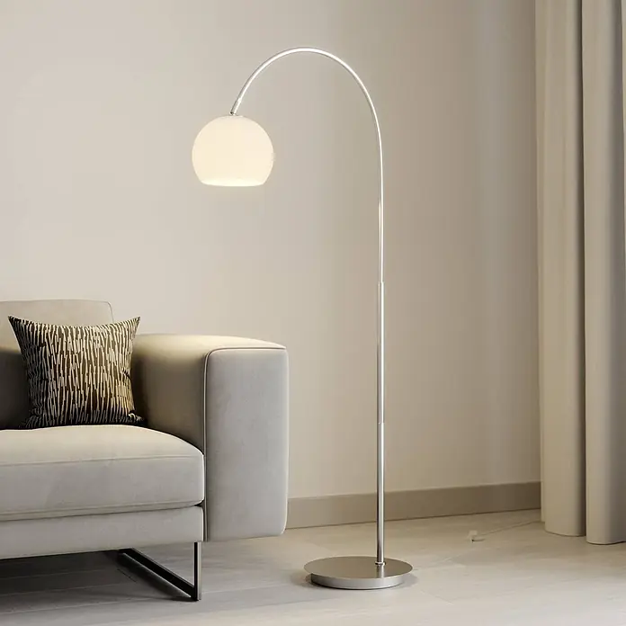 Lindby Stehleuchte Cynthia - alu / grau / zink, E27 - Moderne Bogenstehlampe aus Chrom mit weißem Kugelschirm, neben einem grauen Sofa platziert.