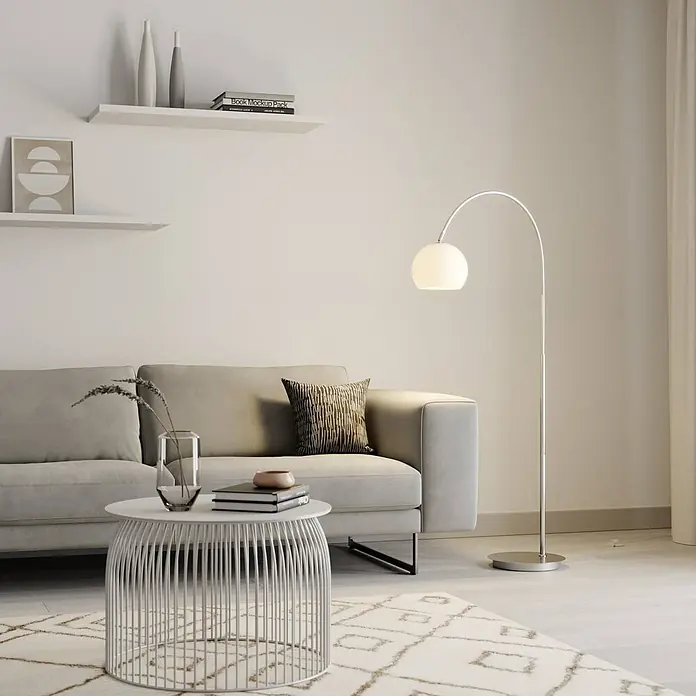 Lindby Stehleuchte Cynthia - alu / grau / zink, E27 - Bogenstehleuchte aus Chrom mit weißem Kugelschirm, beleuchtet ein modernes Wohnzimmersofa.