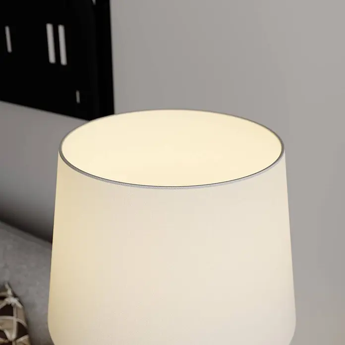 Lindby Stehleuchte Benjiro - chrom / silber, weiß / opal, E27 - Nahaufnahme einer beleuchteten Tischlampe mit beigem Stoffschirm.