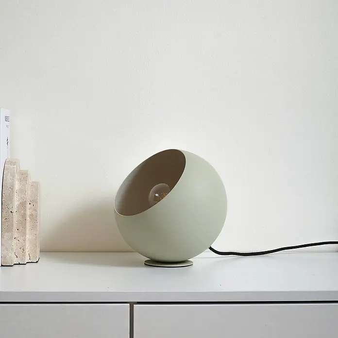 Lindby Tischleuchte Solomia - L x B x H: 20 x 20 x 20 cm, grün, E27 - Hellgrüne kugelförmige Tischlampe mit offener Vorderseite, die die Glühbirne zeigt, neben Steinbuchstützen.