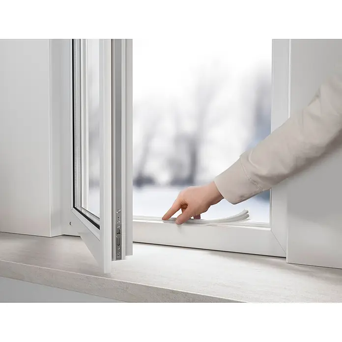 Tesa INSULATION Dichtungsband Gummi S - Weiß, 10 m x 9 mm x 4 mm, Geeignet für: Spaltenbreiten 1 - 3,5 mm - Eine Hand stellt eine weiße flexible Dichtung an einem teilweise geöffneten modernen weißen Fenster ein. Eine verschwommene Schneelandschaft ist sichtbar.