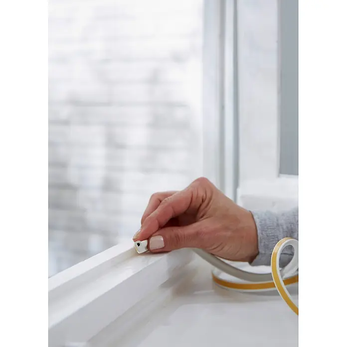 Tesa INSULATION Dichtungsband GUMMI L - Weiß, 10 m x 9 mm x 5,5 mm, Geeignet für: Spaltenbreiten 2 - 5 mm - Hand befestigt weißes D-Profil-Dichtungsband mit gelbem Kleber an Fensterrahmen.