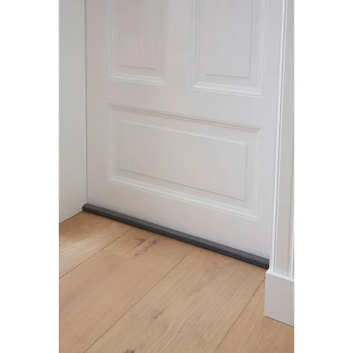 Tesa INSULATION Türbodendichtung Doppel-Dichtung - Grau, 0,95 m x 25 mm, Geeignet für: Glatte Böden - Dunkelgrauer Türdichtungsstreifen am unteren Rand einer weißen Tür auf hellem Holzboden.
