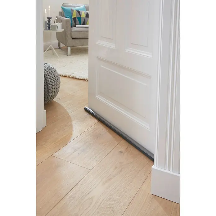 Tesa INSULATION Türbodendichtung Doppel-Dichtung - Grau, 0,95 m x 25 mm, Geeignet für: Glatte Böden - Grauer Zugluftstopper unter einer geöffneten weißen Tür auf Holzboden.