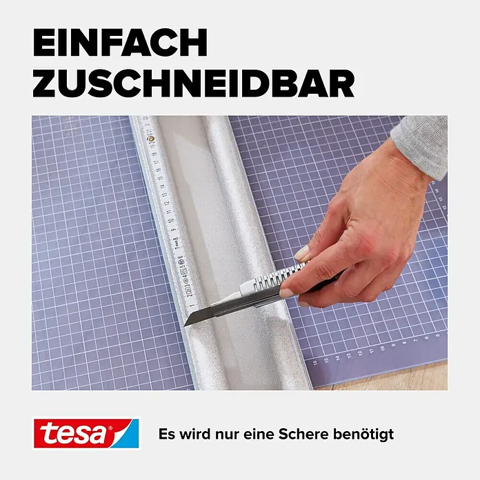 Tesa INSULATION Türbodendichtung Doppel-Dichtung - Weiß, 0,95 m x 25 mm, Geeignet für: Glatte Böden - Hand schneidet silbernes Schaummaterial mit einem Cuttermesser auf einer Schneidematte.