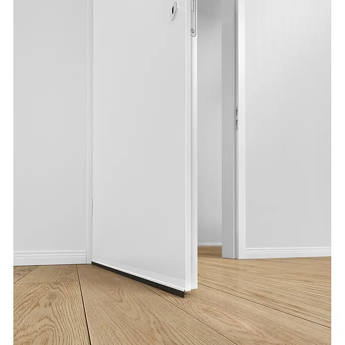 Tesa INSULATION Türdichtschiene für glatte Böden - Weiß, 1 m x 37 mm, Geeignet für: Spaltenbreiten bis 12 mm - Schwarze Bürstendichtung an der Unterseite einer weißen Innentür, die einen Holzboden berührt.
