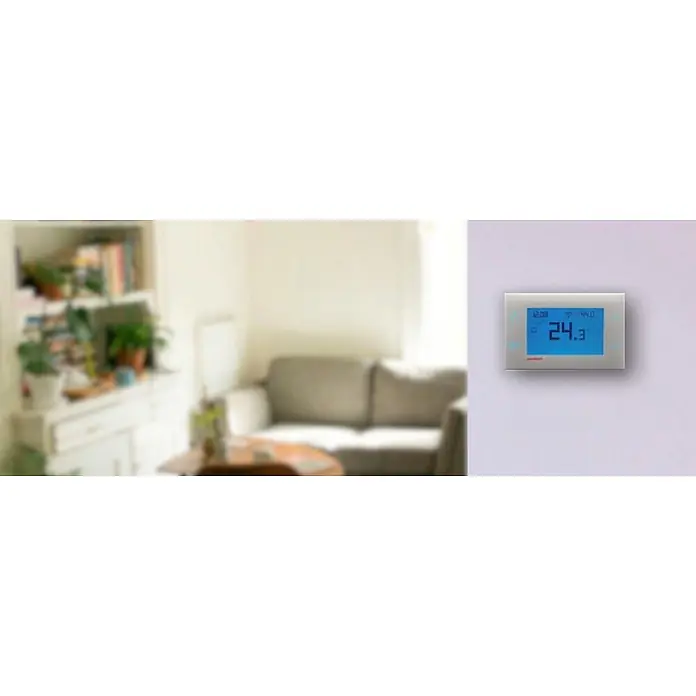 Cronotermostato digital CT-H100 - Regulador de temperatura y humedad - Termostato digital plateado montado en la pared, mostrando 24.3°C, en un entorno de sala de estar difuminado.