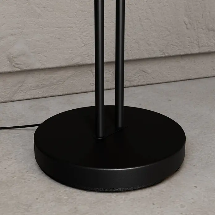 Lucande Stehleuchte Medira - schwarz, schwarz, GU10 - Schwarzer, runder Lampenfuß mit zwei vertikalen Metallstangen und einem Stromkabel auf Betonboden.