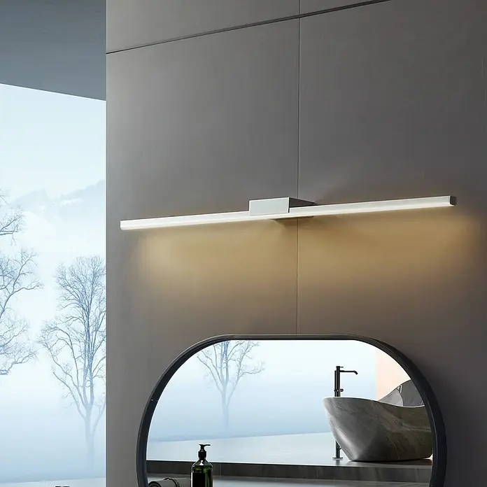 Lucande Wandleuchte Kivana - chrom / silber, chrom / silber - Schlanke, silberne lineare LED-Spiegelleuchte beleuchtet einen ovalen Spiegel in einem modernen Badezimmer.