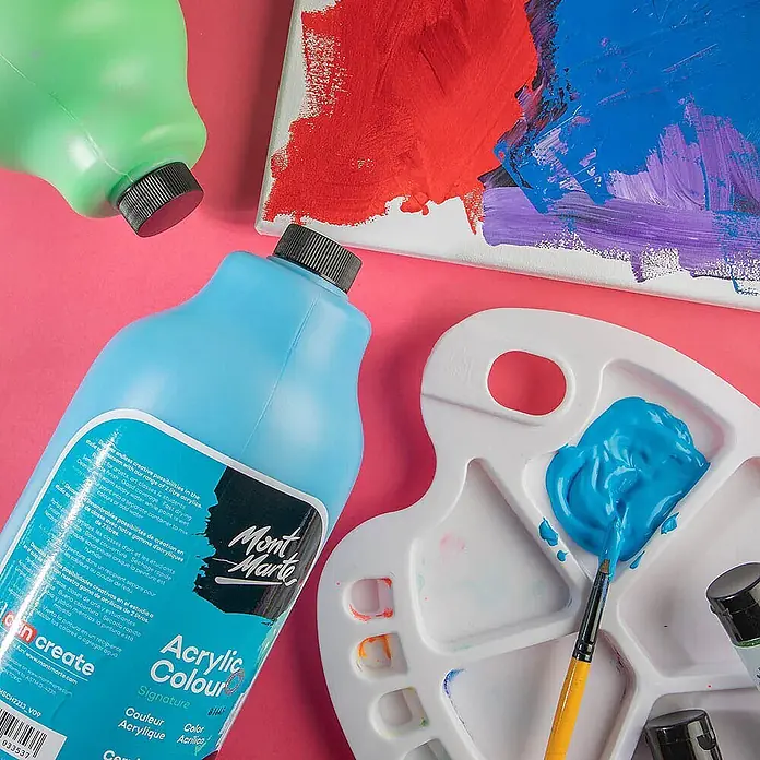 Mont Marte Acrylfarbe Signature - Ceruleanblau, 2.000 ml, Flasche mit Tropfpipette - Große blaue und grüne Acrylfarbenflaschen, eine weiße Palette mit Farbe, ein Pinsel und eine bemalte Leinwand auf pinkem Untergrund.