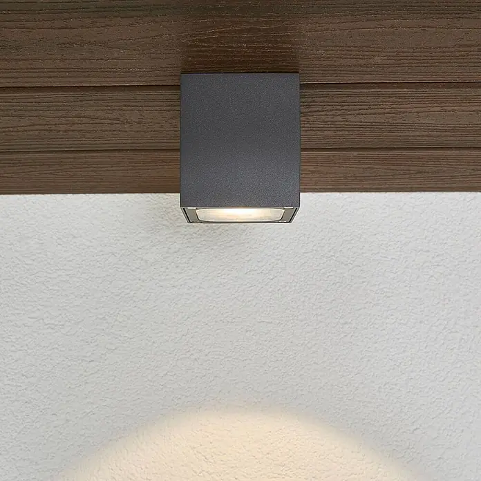 Lucande Außenwand- & Deckenleuchte Tanea - alu / grau / zink, alu / grau / zink, IP54 - Quadratische dunkelgraue Außenleuchte, an Holzbalken montiert, beleuchtet eine strukturierte Wand.