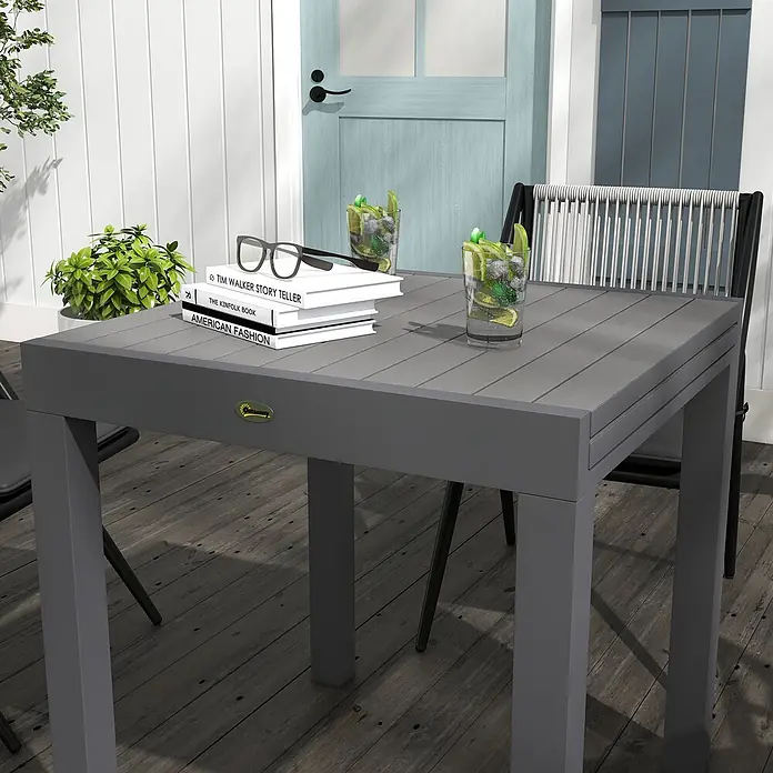 Outsunny Gartentisch - Aluminium, Quadratisch, Grau - Grauer Lamellen-Esstisch für den Außenbereich mit quadratischen Beinen, der erfrischende Getränke und Bücher in einem Outdoor-Ambiente zeigt.