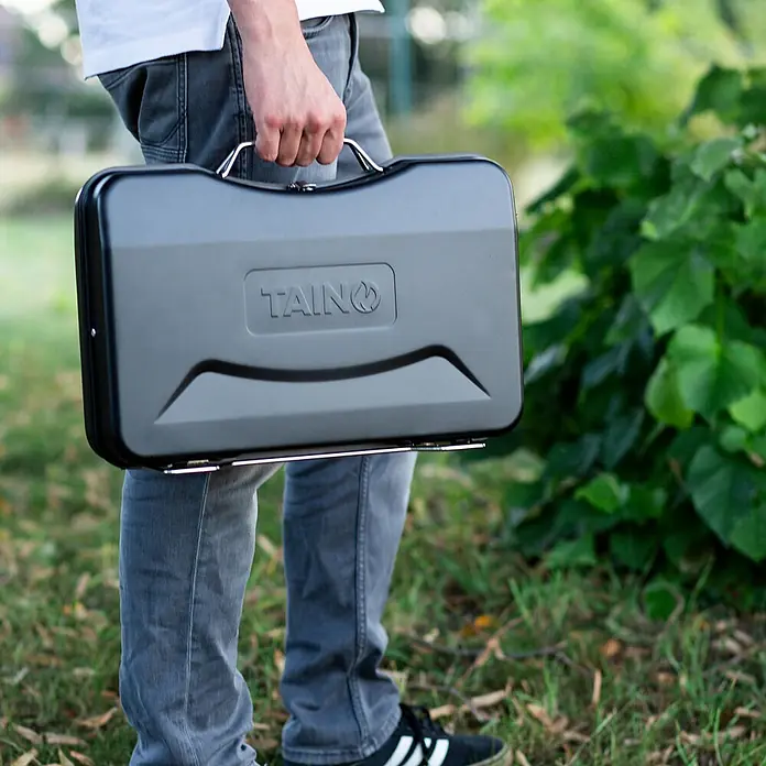 TAINO Holzkohlegrill MOX - Schwarz - Person trägt einen schwarzen, rechteckigen TAINQ Portabelgrill.