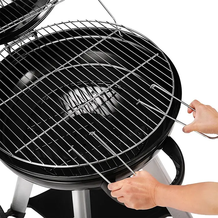 TAINO Holzkohlegrill NEO - Durchmesser Grillfläche: 54 cm, Schwarz - Runder schwarzer Holzkohlegrill mit verchromtem Rost. Eine Hand hebt den Rost mit einem Werkzeug an.