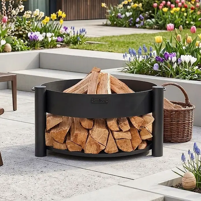 Bene on Fire Holzkohlegrill Washington - Schwarz - Schwarze Metall-Feuerschale und Holzscheitlager, gefüllt mit Holz, auf einer Terrasse im Garten.
