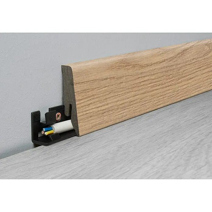 LOGOCLIC Aquaprotect Sockelleiste K58 Soft Oak - 260 cm x 18 mm x 58 mm, MDF/HDF - Eine Sockelleiste mit integriertem Kabelkanal zur diskreten Kabelführung entlang der Wand. Die Leiste ist aus hellem Holz.