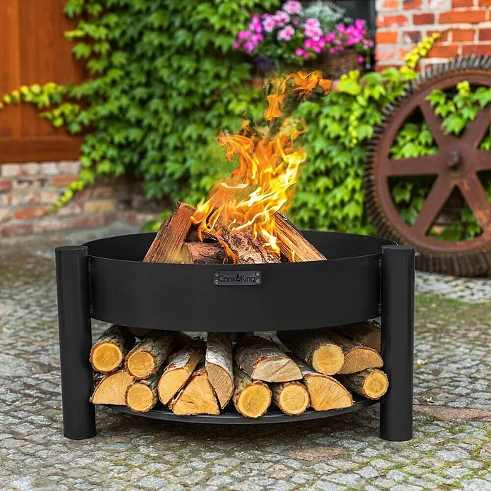 Bene on Fire Holzkohlegrill Washington - Schwarz - Schwarze Metall-Feuerschale mit brennendem Feuer und Holzablage im Freien.