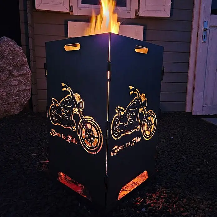 TiKo-Design Holzkohlegrill Feuerkorb-Born to ride - silbergrau - Dunkle Metall-Feuerschale mit Motorrad-Aussparungen und "Born to Ride"-Schriftzug, brennt nachts im Freien.