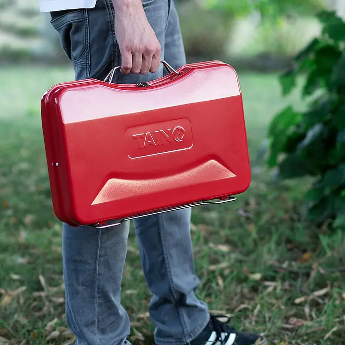 TAINO Holzkohlegrill MOX - Rot - Roter TAINQ tragbarer Grill im Kofferstil, von einer Person getragen. Mit Metallgriff.